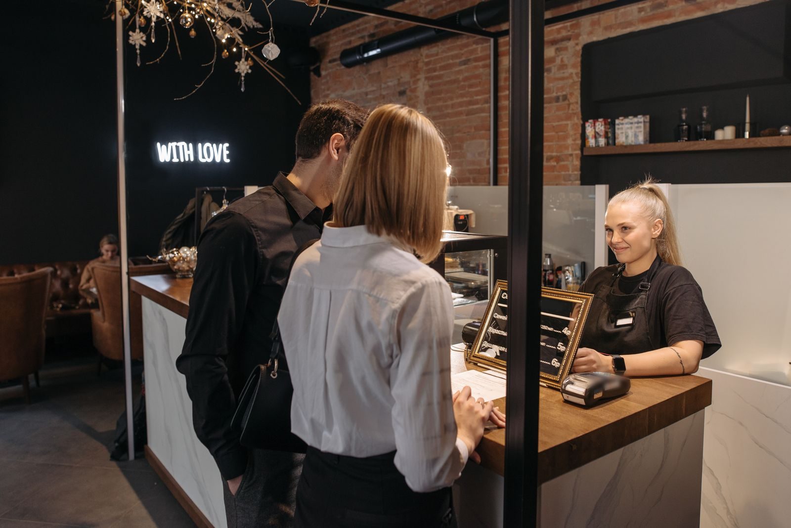 Customers paying at the counter of a small cafe while a staff member assists them